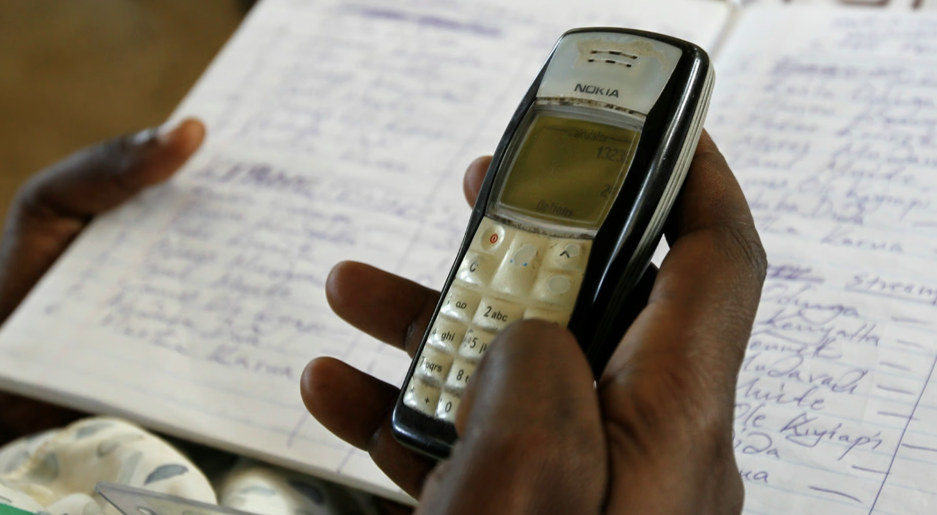 A hand holding a basic mobile phone over a handwritten paper register